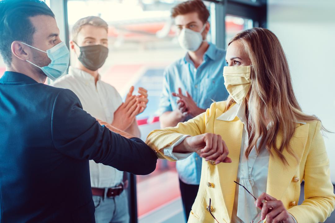 Menschen, die Gesichtsmasken tragen, begrüßen sich mit einem Ellbogenstoß in einem Büro.